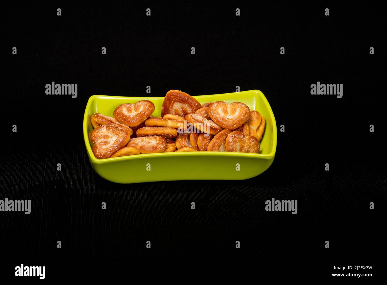 Hearts Shaped Biscuit In Green Square Bowl, Biscuits Heap, Isolated on Black Background Stock Photo
