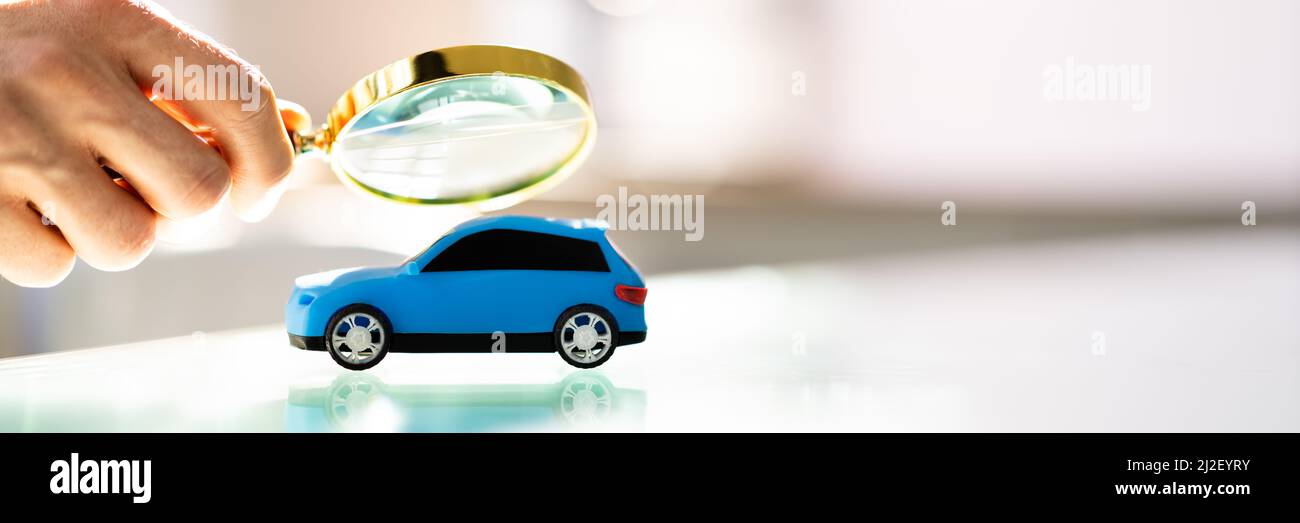 Person Scrutinizing A Car Model Using Magnifying Glass On Desk Stock Photo