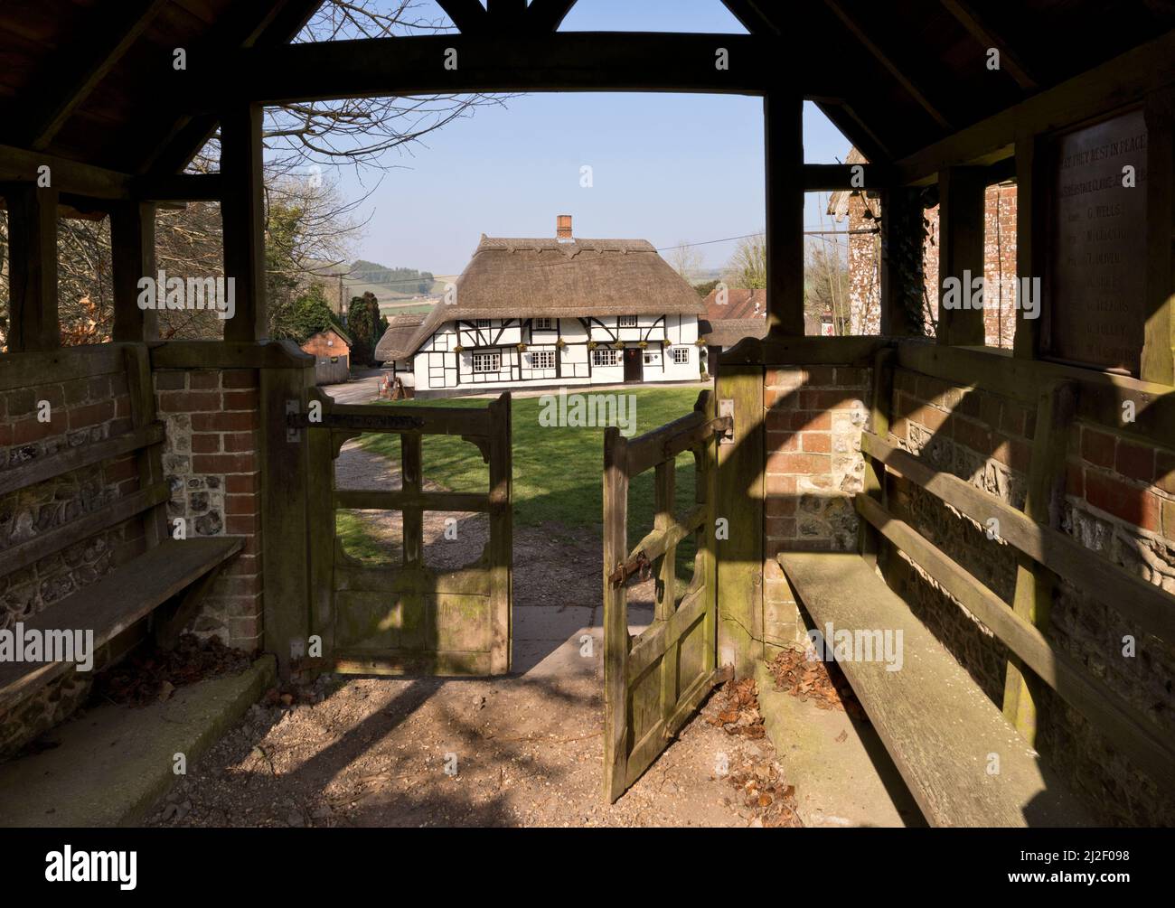 The Hampshire village of Hampshire. The thatched Red Lion pub is seen through the lychgate of St Michael and All Angels parish church. Stock Photo
