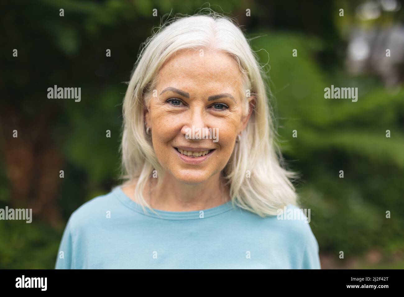 Portrait of smiling caucasian senior woman with white hair standing in backyard Stock Photo