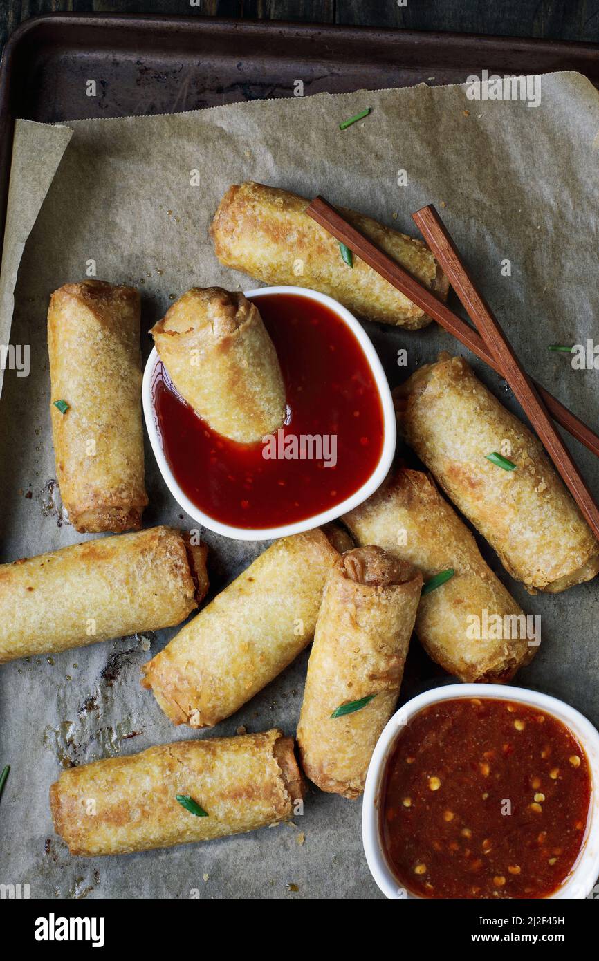 Top view of egg rolls in sweet and sour sauce over a dark rustic table with chop sticks. Garnished with green onions. Overhead table top view. Stock Photo