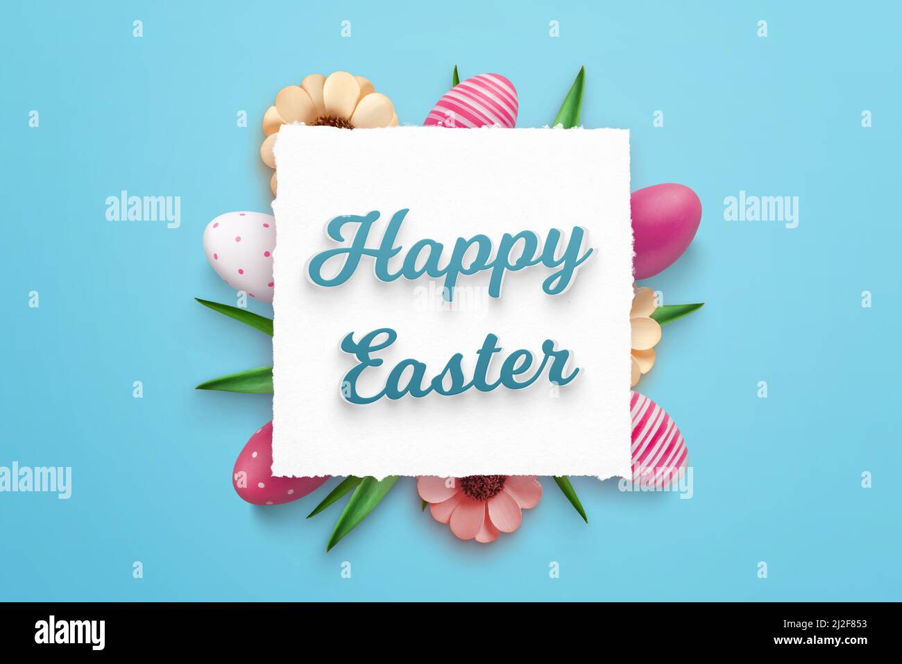Happy Easter greeting card on square paper surrounded by Easter decorations. Blue background, top view, flat lay Stock Photo