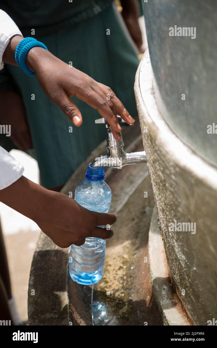 School student filling up refillable plastic water bottle from a fountain in their school courtyard in Oshana Region, Namibia, Africa. Stock Photo