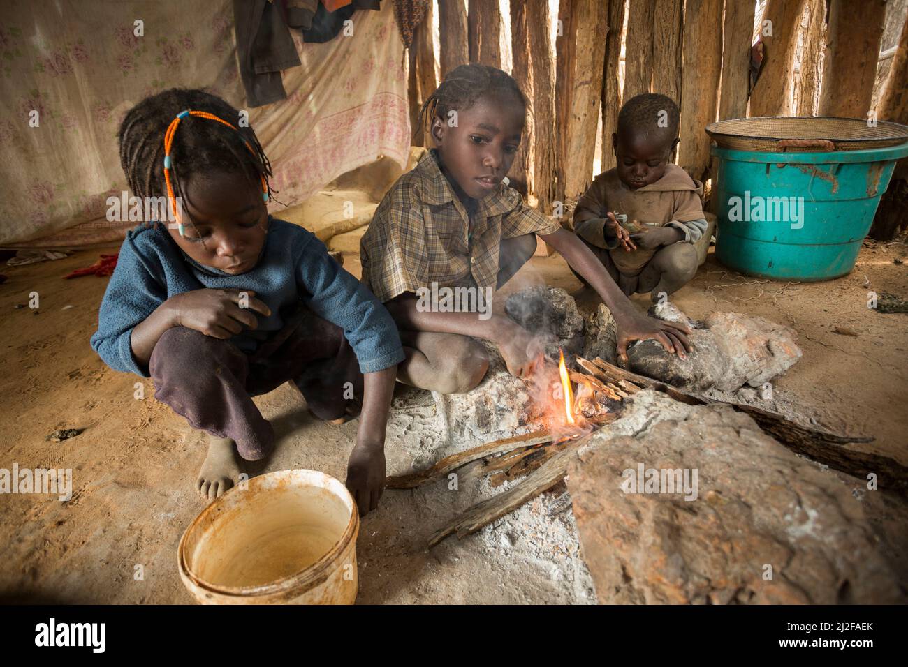 Three children warm themselves by the fire in their one room shack in Omusati Region, Namibia, southwest Africa. Stock Photo