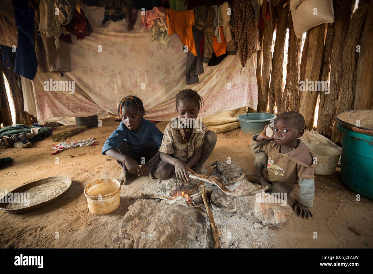 Three children warm themselves by the fire in their one room shack in Omusati Region, Namibia, southwest Africa. Stock Photo