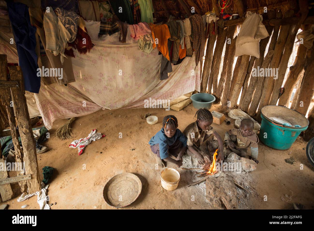 Three children warm themselves by the fire in their one room shack in