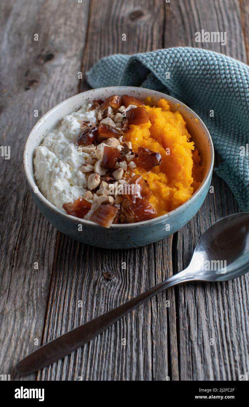 Fitness breakfast bowl with high protein cottage cheese, pumpkin puree, dates and nuts. Served with spoon isolated on wooden table with 'copy space' Stock Photo