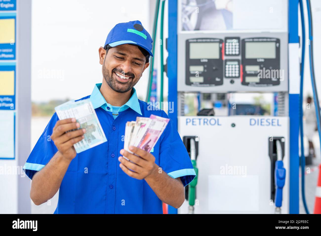 Smiling gas filling station attendant counting money at petrol pump - concept of business profit, earnings, salary and finance Stock Photo