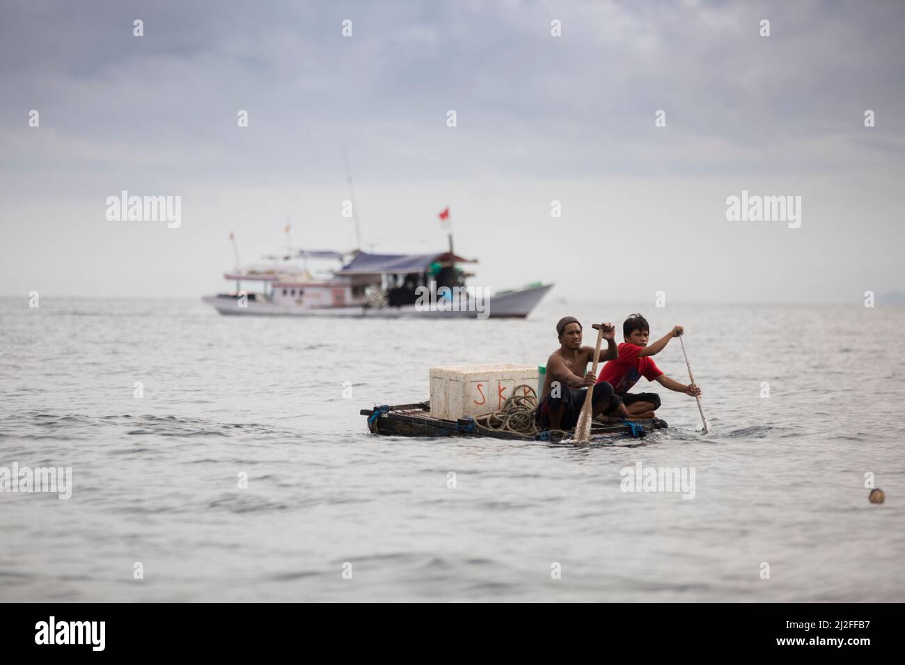 Two fishermen paddle a small raft out to sea from the city of Mamuju, West Sulawesi, Indonesia, Asia. Stock Photo