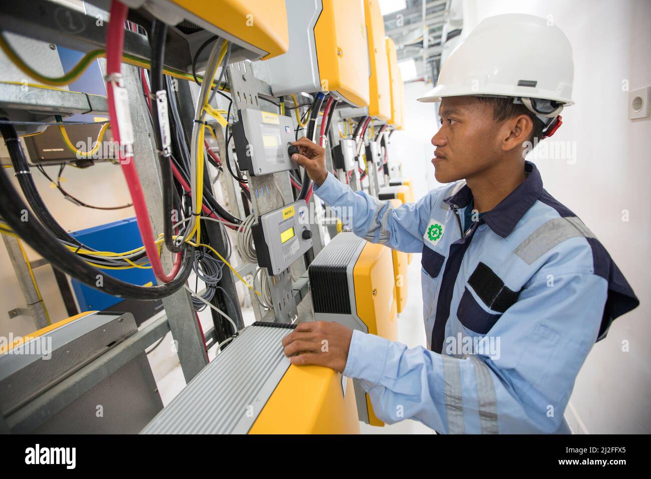 Junior electrical technician, Askari (28), operates equipment at a solar electricity plant on Karampuang Island, Indonesia, which was commissioned as Stock Photo