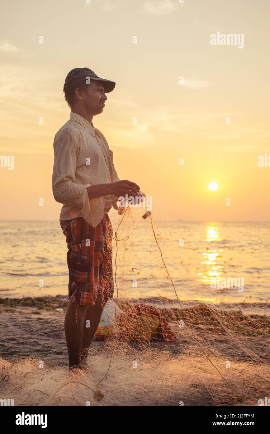 Kochi, India - Junuary 22, 2015: Indian fisherman catches fish by the traditional method of throwing net into the sea at sunset. Kerala region. Stock Photo