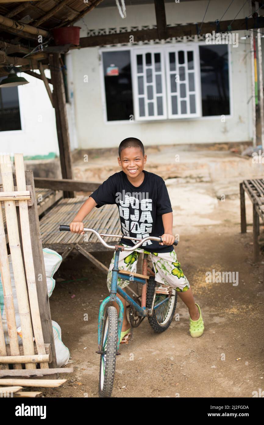 A smiling boy rides a bicycle on the small remote island of Karampuang, Indoneisa, off the coast of Mamuju, Sulawesi. Stock Photo