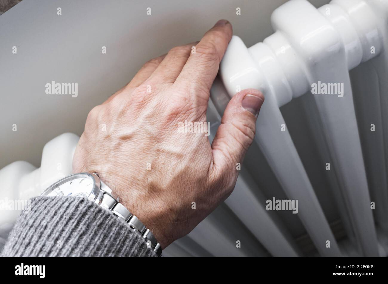 Male hand touching white home radiator, close up photo with selective focus. Modern house heating technology Stock Photo