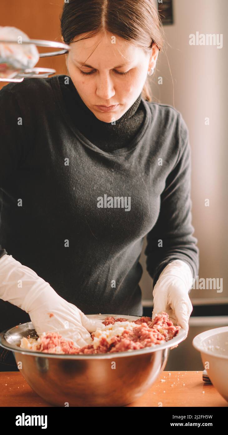 A vertical shot of a female chef mixing a meat mixture in the kitchen with rubber gloves on