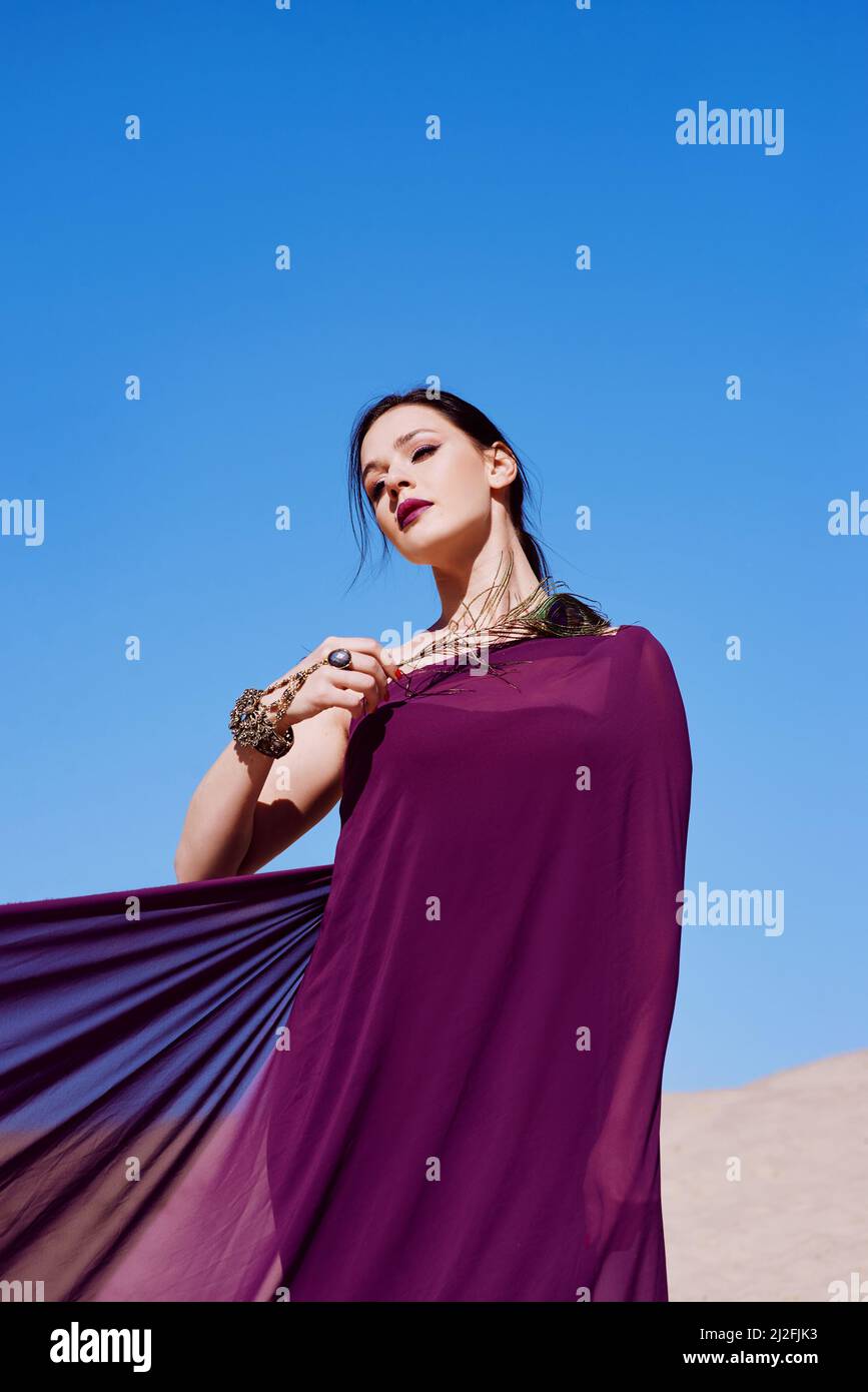 Amazing beautiful brunette woman with the Peacock feather in purple fabric in the desert. Oriental, Indian, fashion, style concept Stock Photo