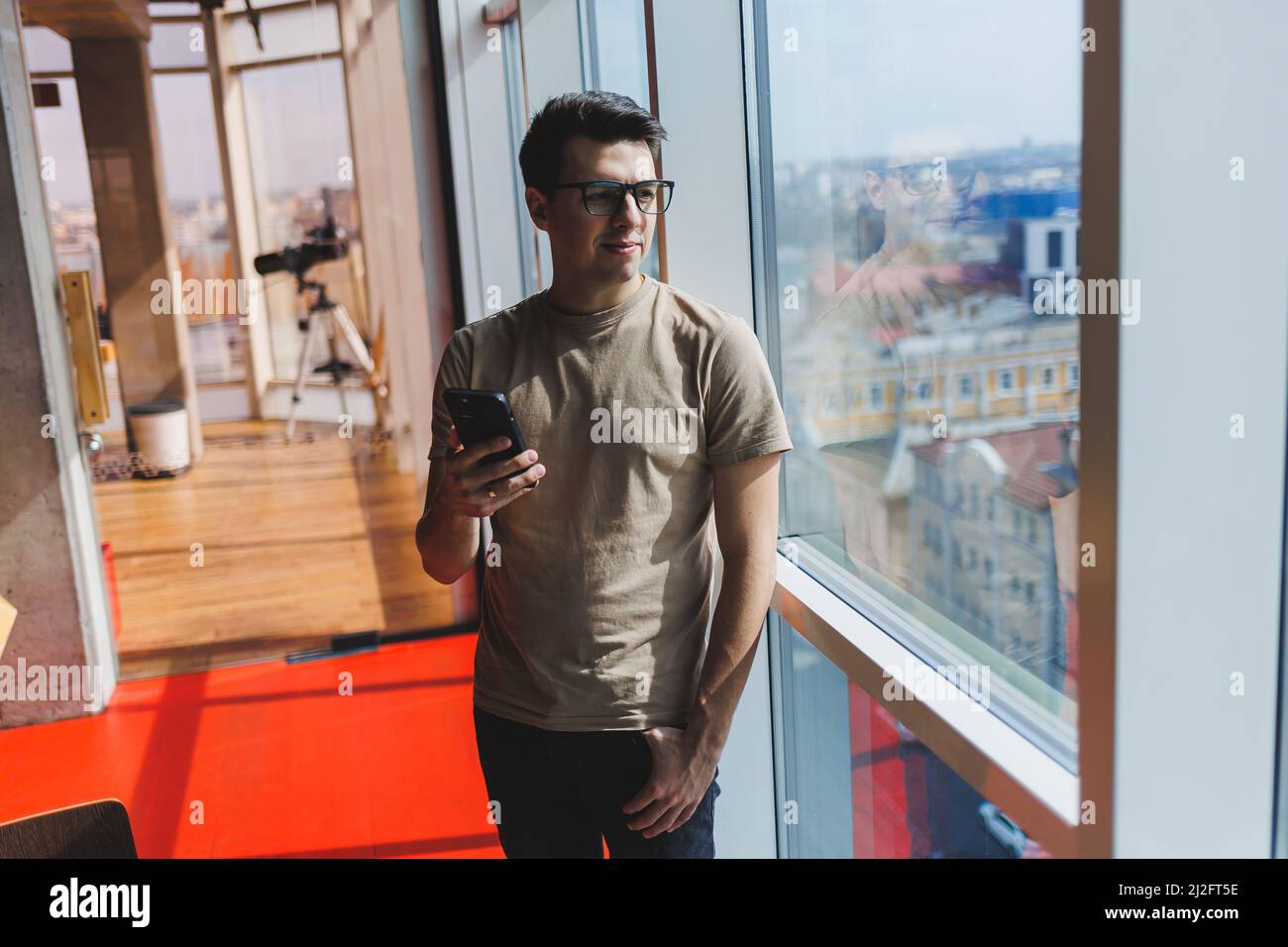 Cheerful scofe male entrepreneur standing near office window and smiling during working day in company, successful corporate boss feeling good from ri Stock Photo