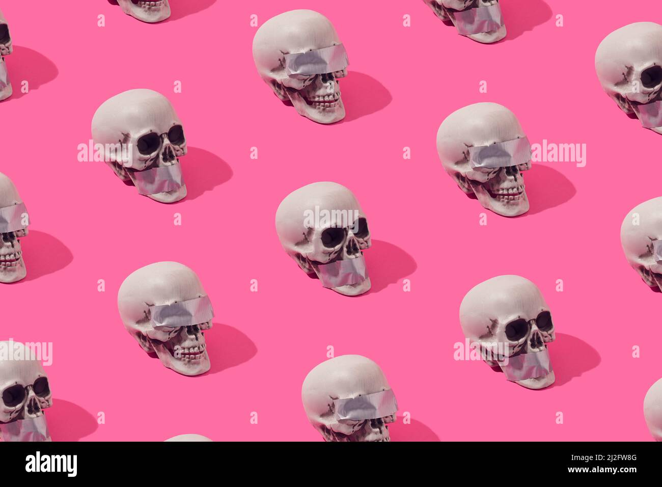 Human skulls with with duct tape over the eyes and mouth on a pink background. Truth and justice illusion pattern. Stock Photo