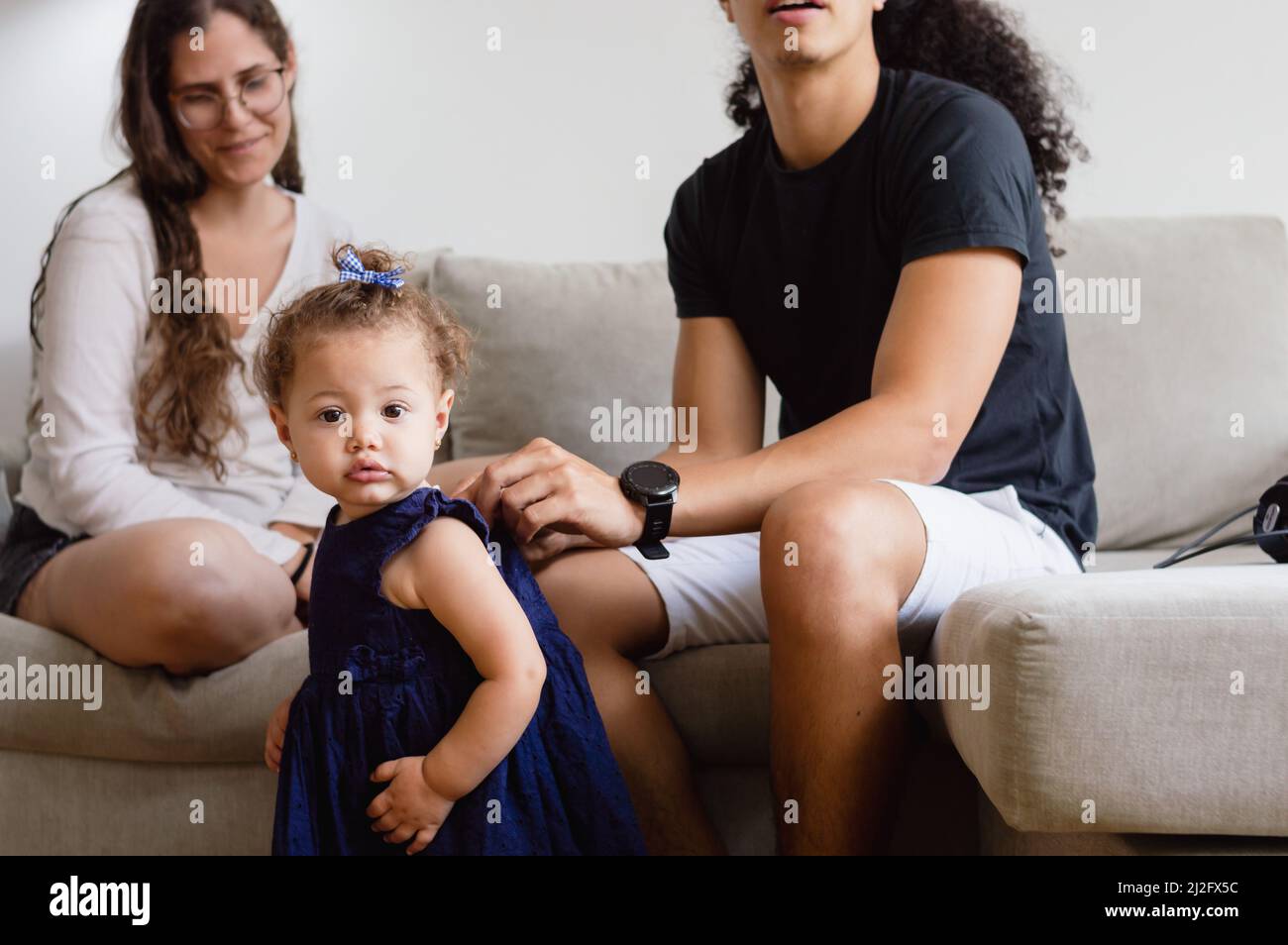 little caucasian baby standing in the living room looking at the camera while her dad finishes dressing her in a blue dress to go out, family and fath Stock Photo