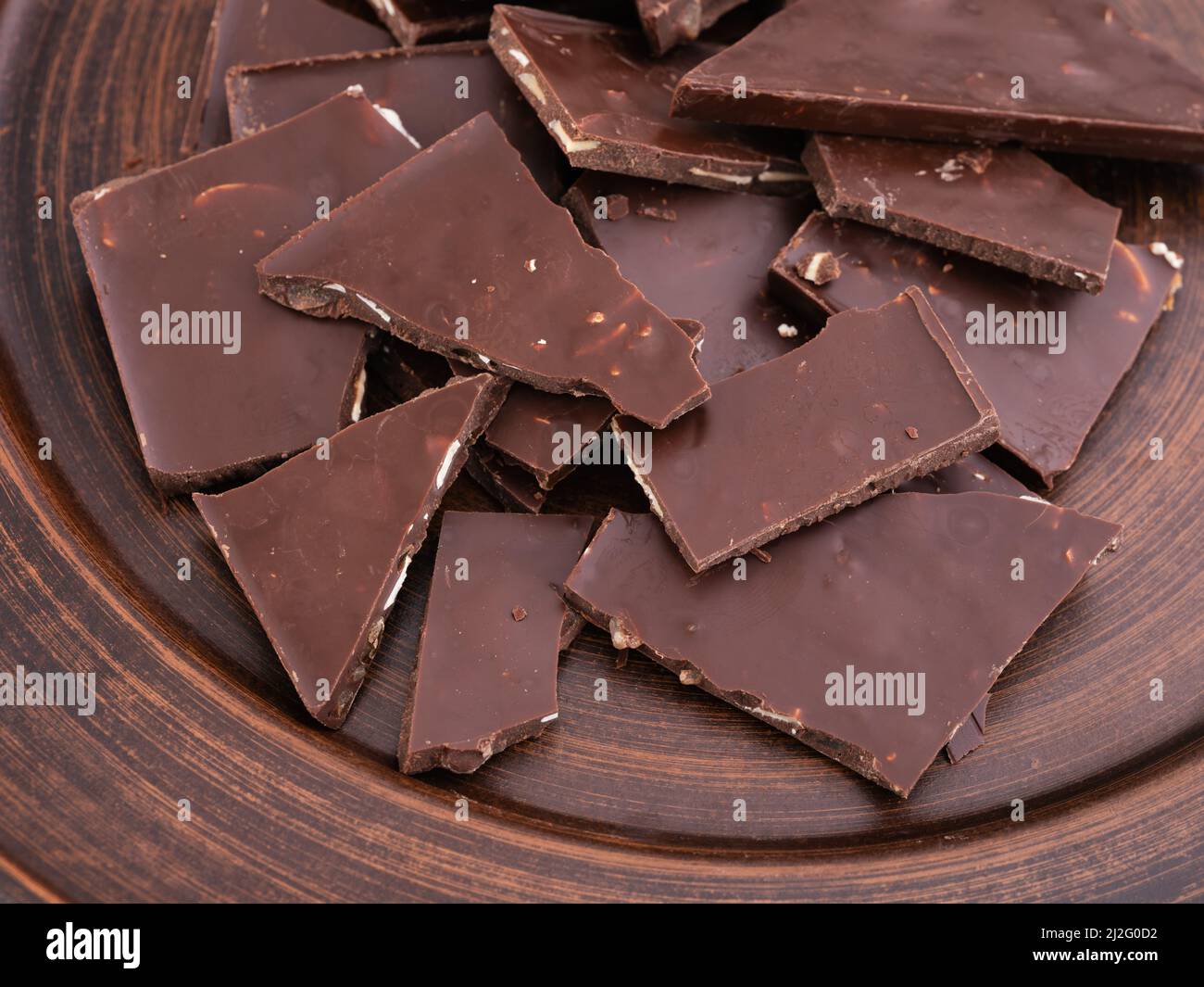 Pieces of broken chocolate bar on a brown plate. Close up Stock Photo
