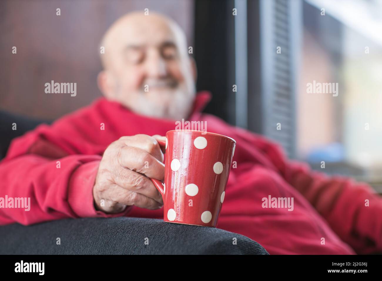 old man sitting in an armchair and drinking coffee Stock Photo