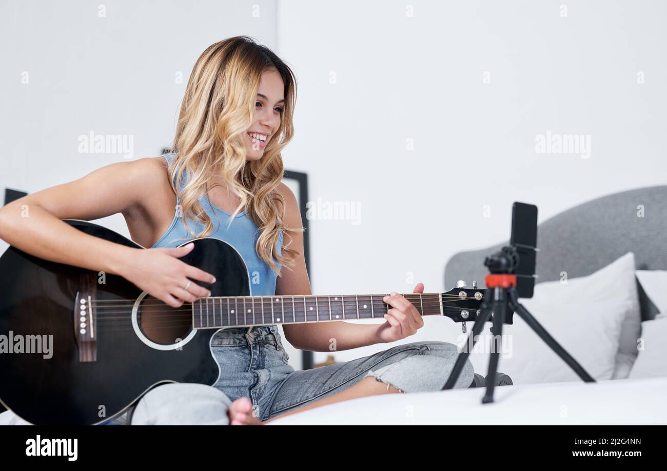 Keep doing what youre doing, you never know who youre inspiring. Shot of a young woman using her cellphone to record herself while playing the guitar Stock Photo