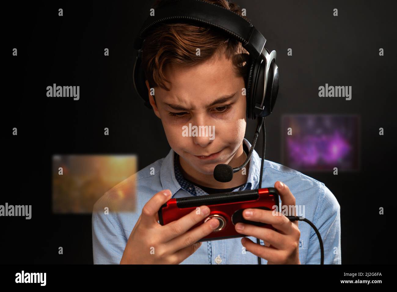 A teenage boy in headphones, intently playing a game on his smartphone. Transparent screens with games in front of the player. Black background. Conce Stock Photo