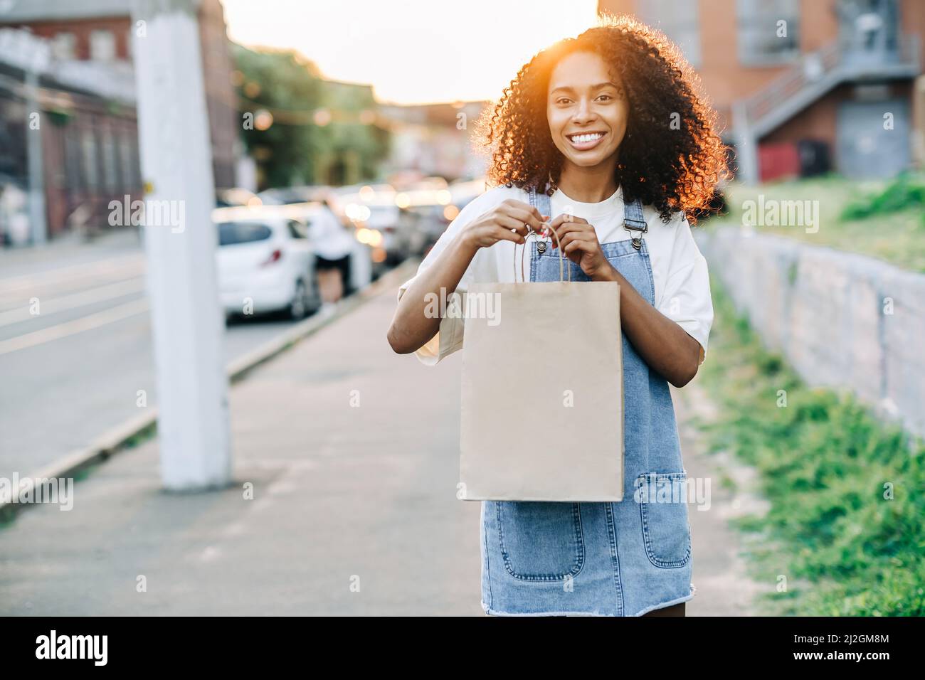Stylish smiling african woman holds craft paper bag outdoors. Takeaway food concept Stock Photo