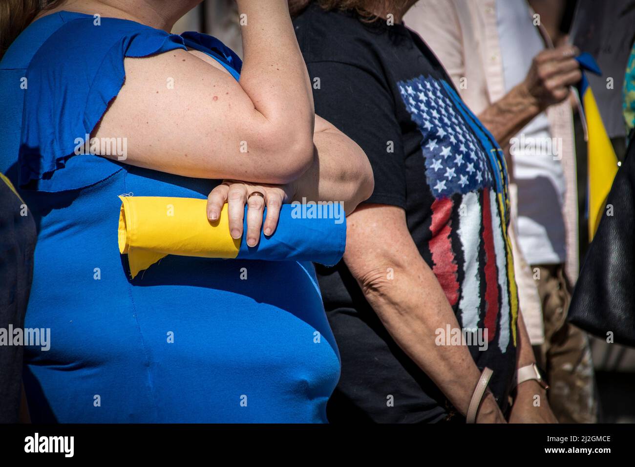 Man and woman with Ukrainian flags stand on either side of woman in USA tee shirt at pro-Ukrainian Rally in Tulsa USA - cropped Stock Photo
