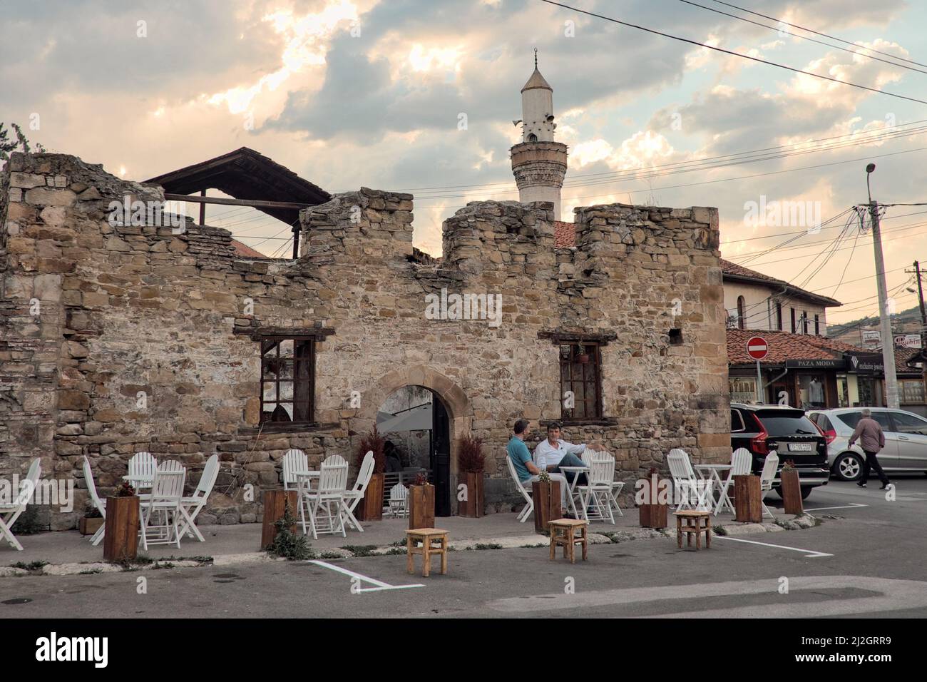NOVI PAZAR, SERBIA - AUGUST 12, 2017: clients sitting on sidewalk of a coffee bar in the old turkish quarter; on background minaret of a mosque agains Stock Photo