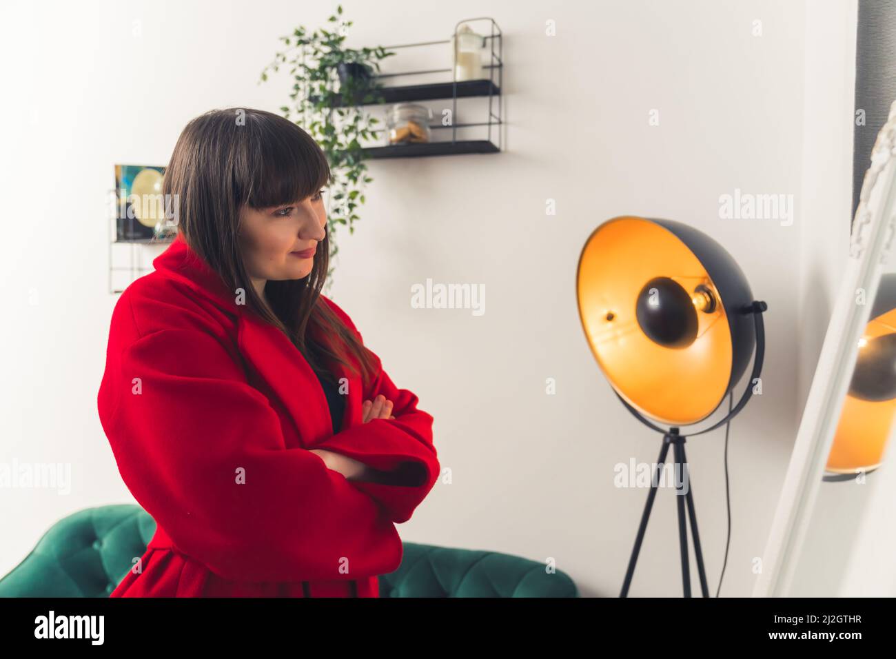 Confident European customer woman looking at herself in the mirror while trying on red winter coat. High quality photo Stock Photo