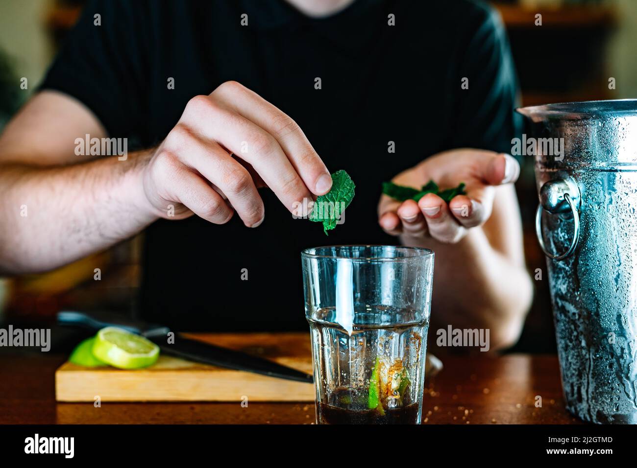 detail of the hands of a young and modern waiter, adding mint in the preparation of a mojito. Stock Photo