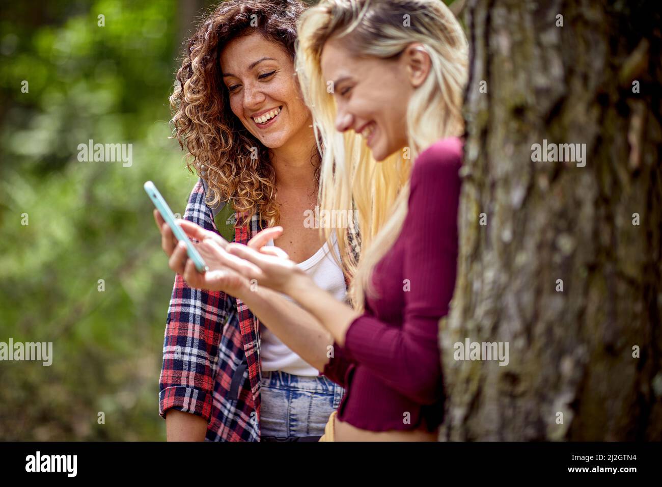 Two young cheerful girls looking at mobile phone and laughing. Summertime, mountain landscape. Freedom, friendship, nature concept. Stock Photo