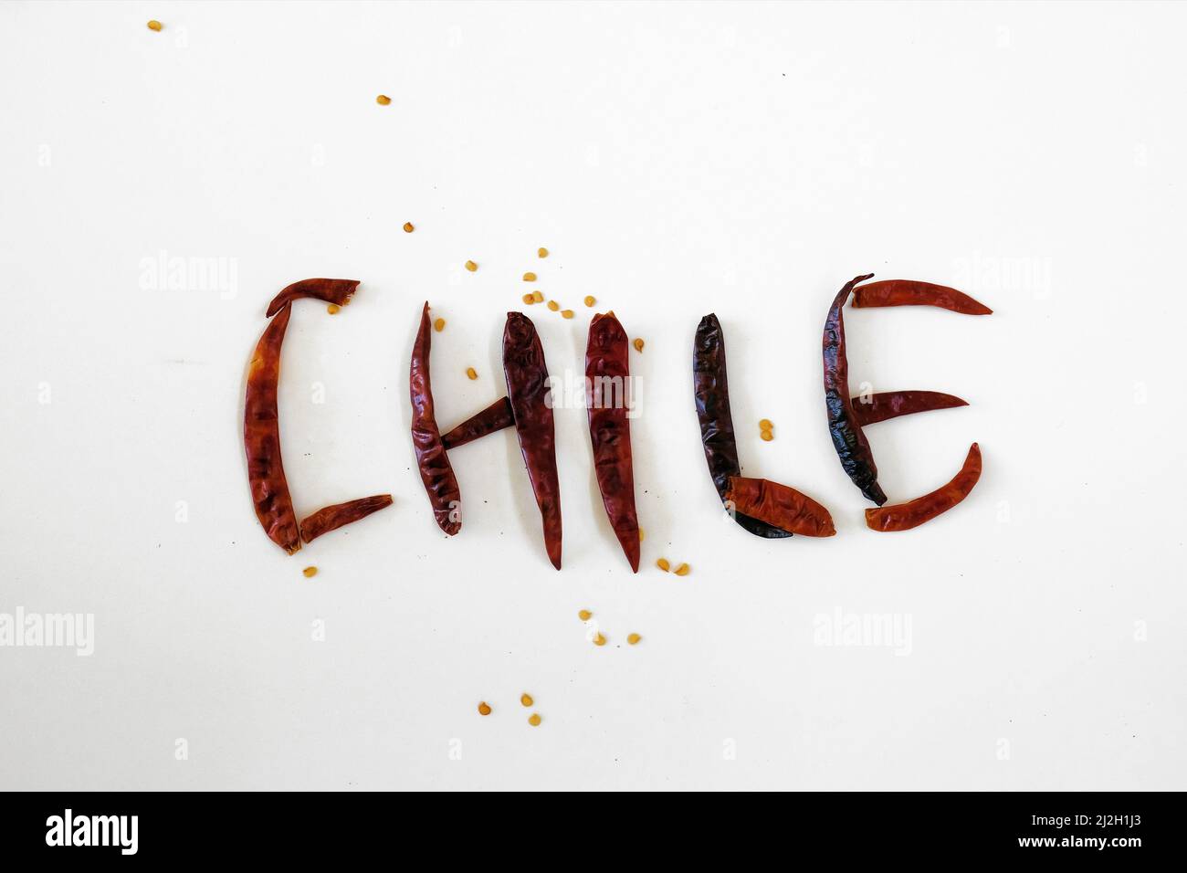 The word Chile spelled out in Spanish with dry roasted chile de arbol peppers on a white surface