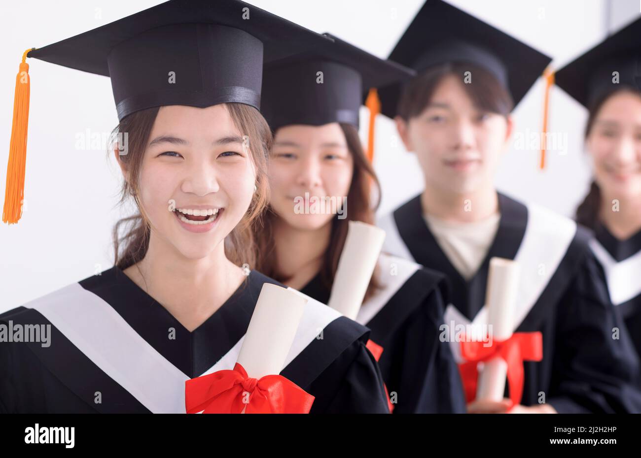 Smiling asian girl student  graduate and classmates standing with diplomas in hands Stock Photo