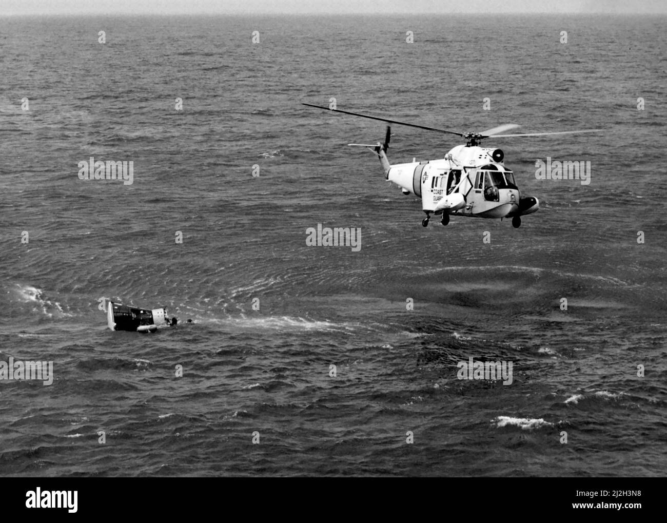 A U.S. Coast Guard Sikorsky HH-52A Seaguard helicopter over the Gemini 3 space capsule flown by astronauts Gus Grissom and John Young after it splashed down in the Atlantic Ocean, 23 March 1965. The aircraft carrier USS Intrepid (CVS-11) recovered the craft and crew. Stock Photo