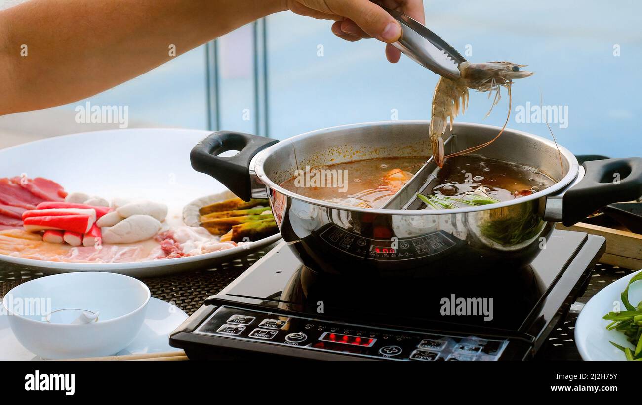 Man hand take river prawn and put it in boiling pot Shabu shabu hotpot