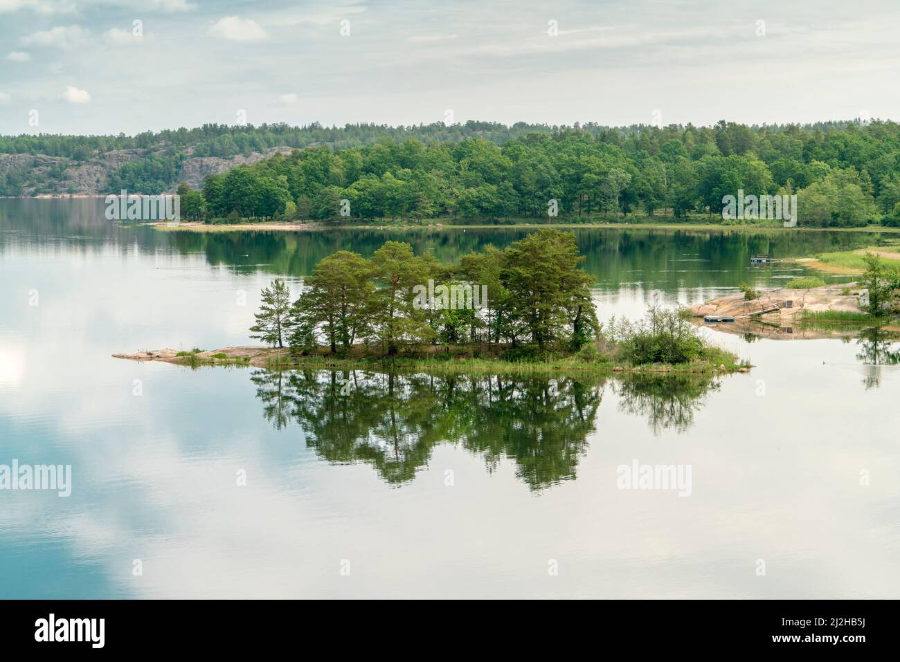 Sweden, Loftahammar, Small island on calm sea trees and clouds Stock Photo