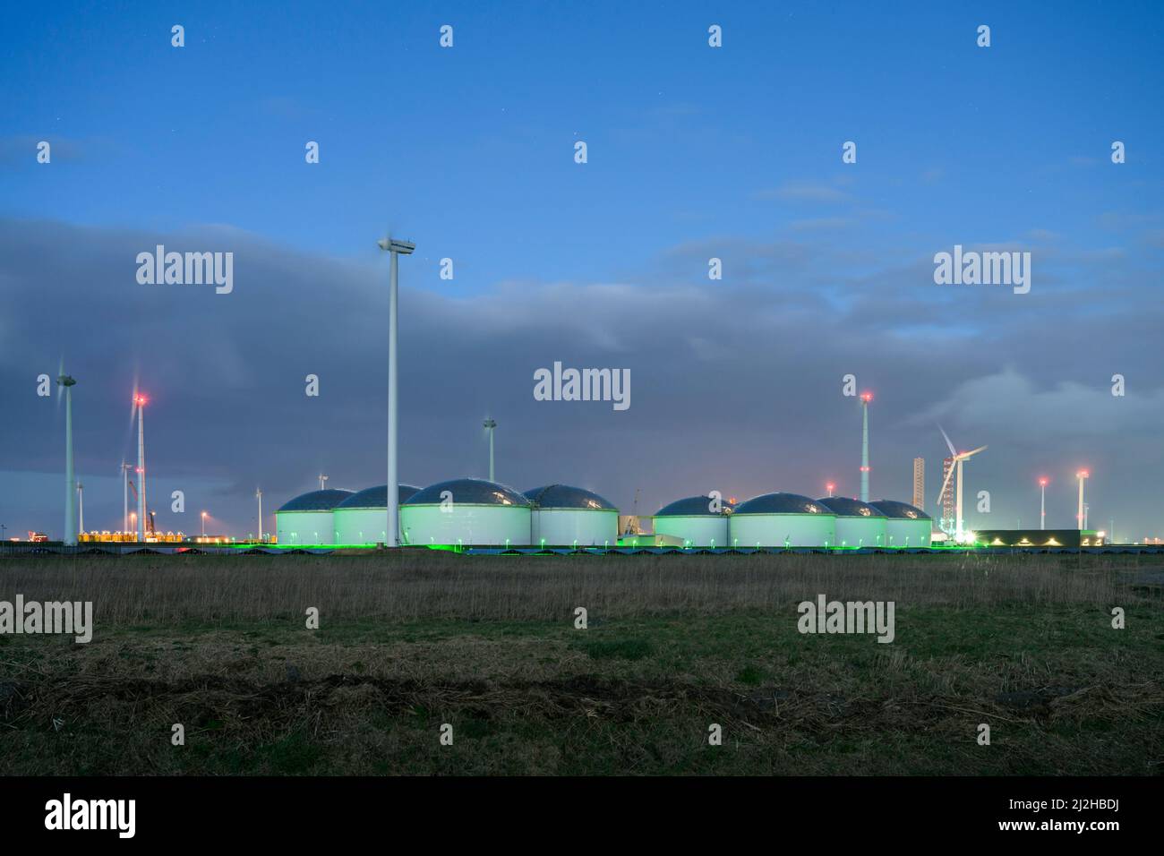 Netherlands, Eemshaven, Wind turbines and storage tanks at dusk Stock Photo