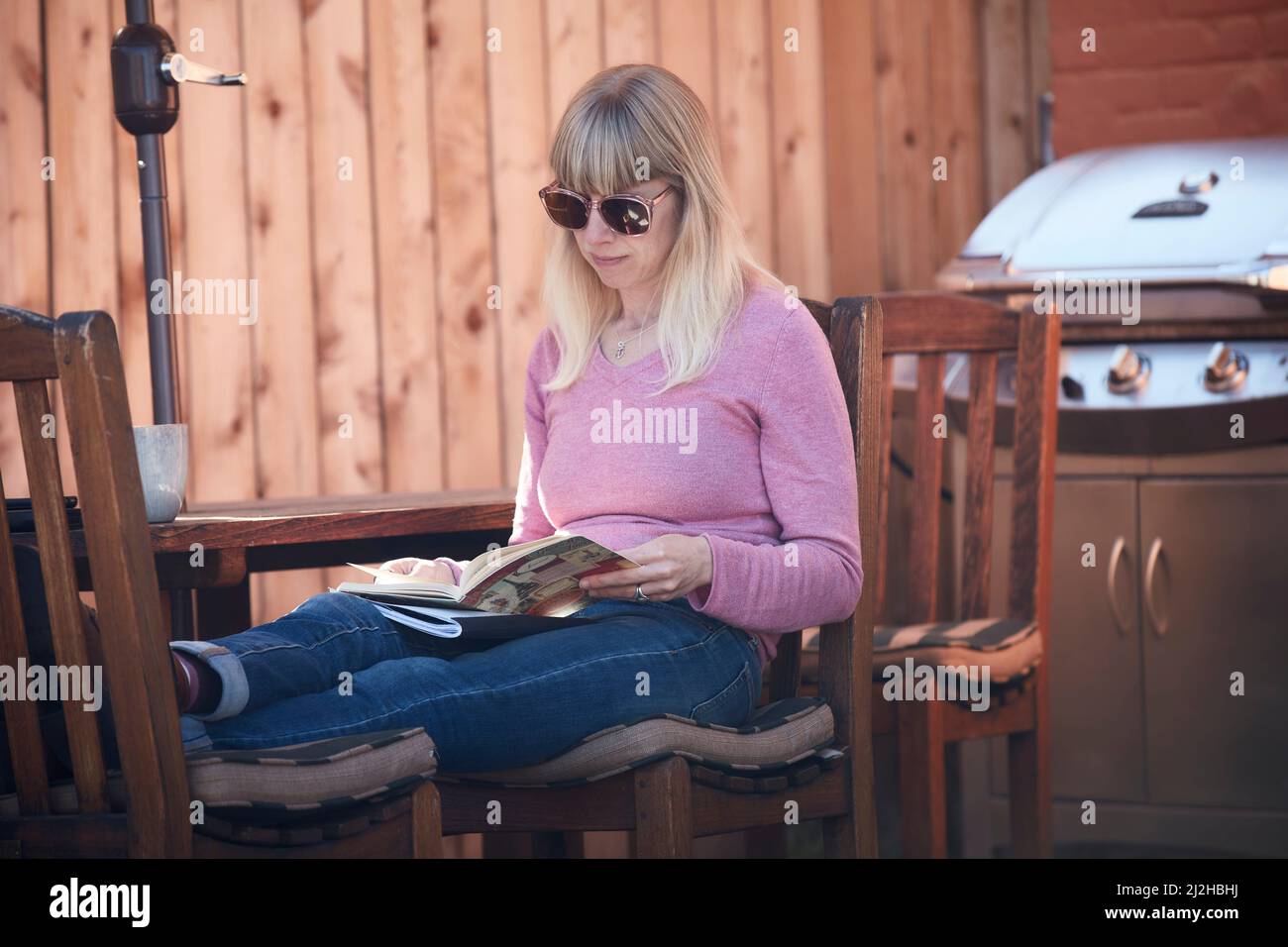 Woman reading book on patio Stock Photo - Alamy