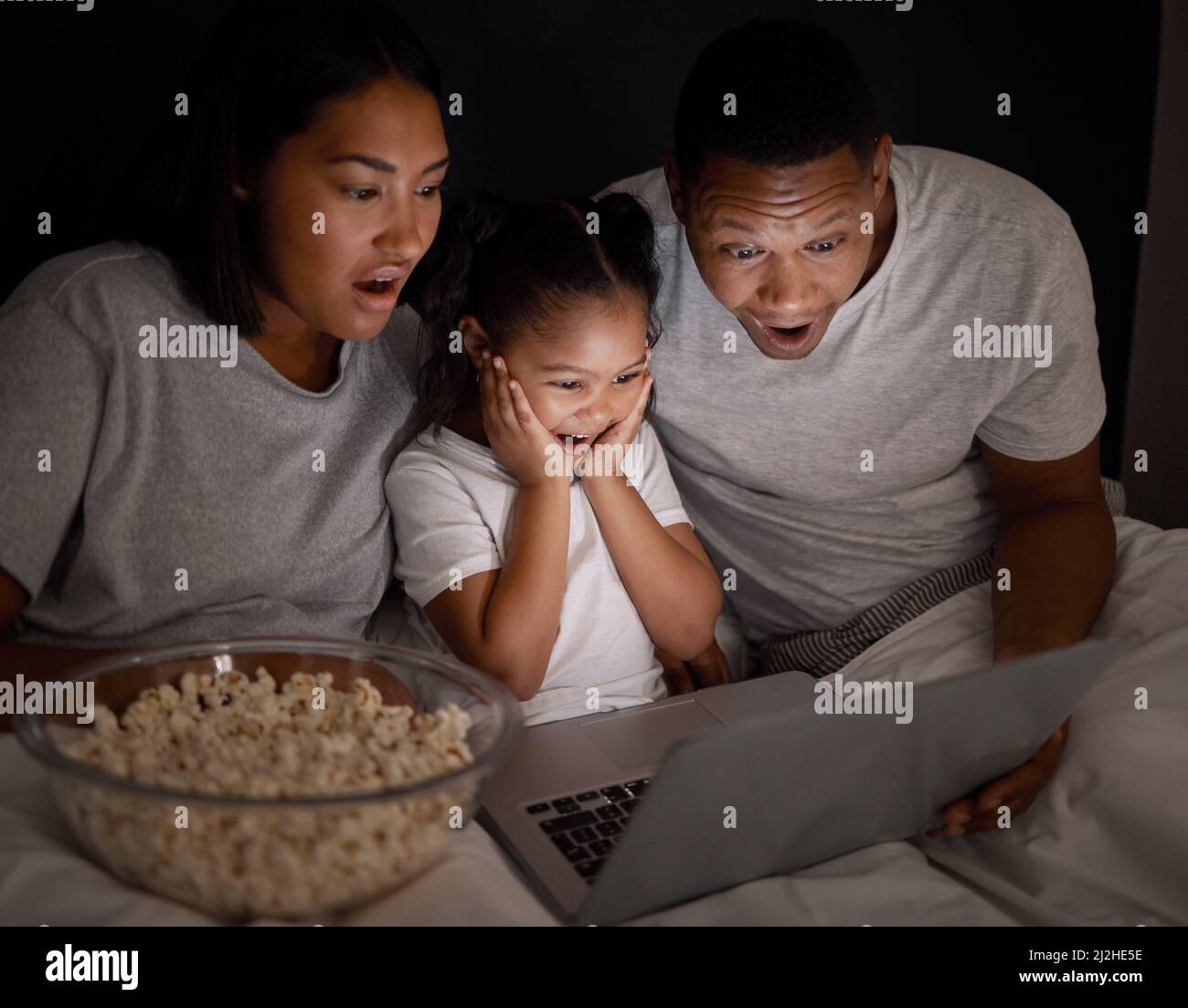 Did you just see that. Shot of a young couple sitting in bed with their daughter and using a laptop at night. Stock Photo