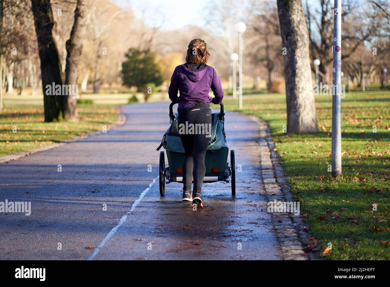Stuttgart, Germany - December 31, 2021: Young woman with stroller jogging alone in the park. Person with purple training clothes moves in nature. Stock Photo
