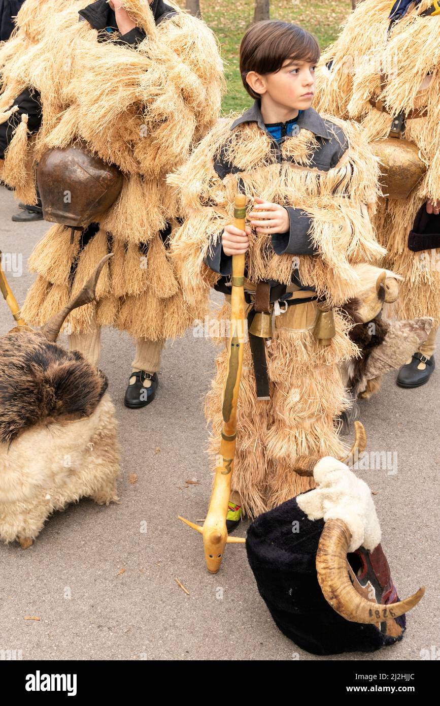 Bulgarian boy at the Kukeri mystical traditional millennium old winter festival in Sofia, Bulgaria, Balkans, Eastern Europe. Kukeri is a centuries-old tradition intended to chase evil spirits away and to invite good, held around early winter or midwinter. The participants wear oversized bells, embroidered costumes and fantastical masks to participate in the winter ritual. Stock Photo