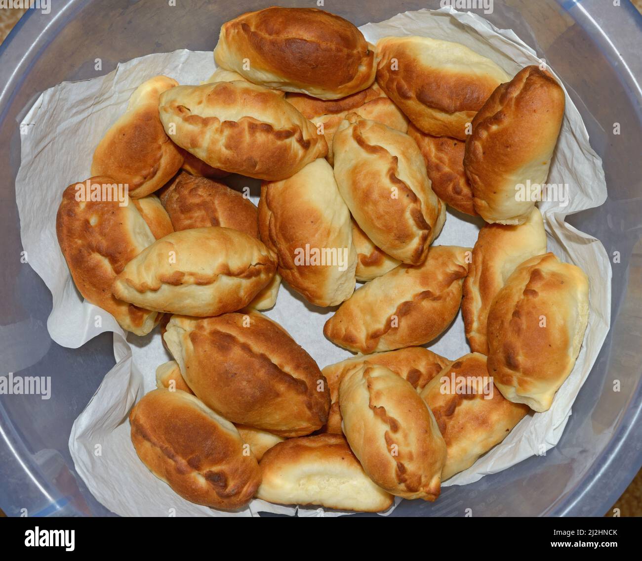 Many traditional Russian baked patties on paper in deep blue plastic bowl. Stock Photo