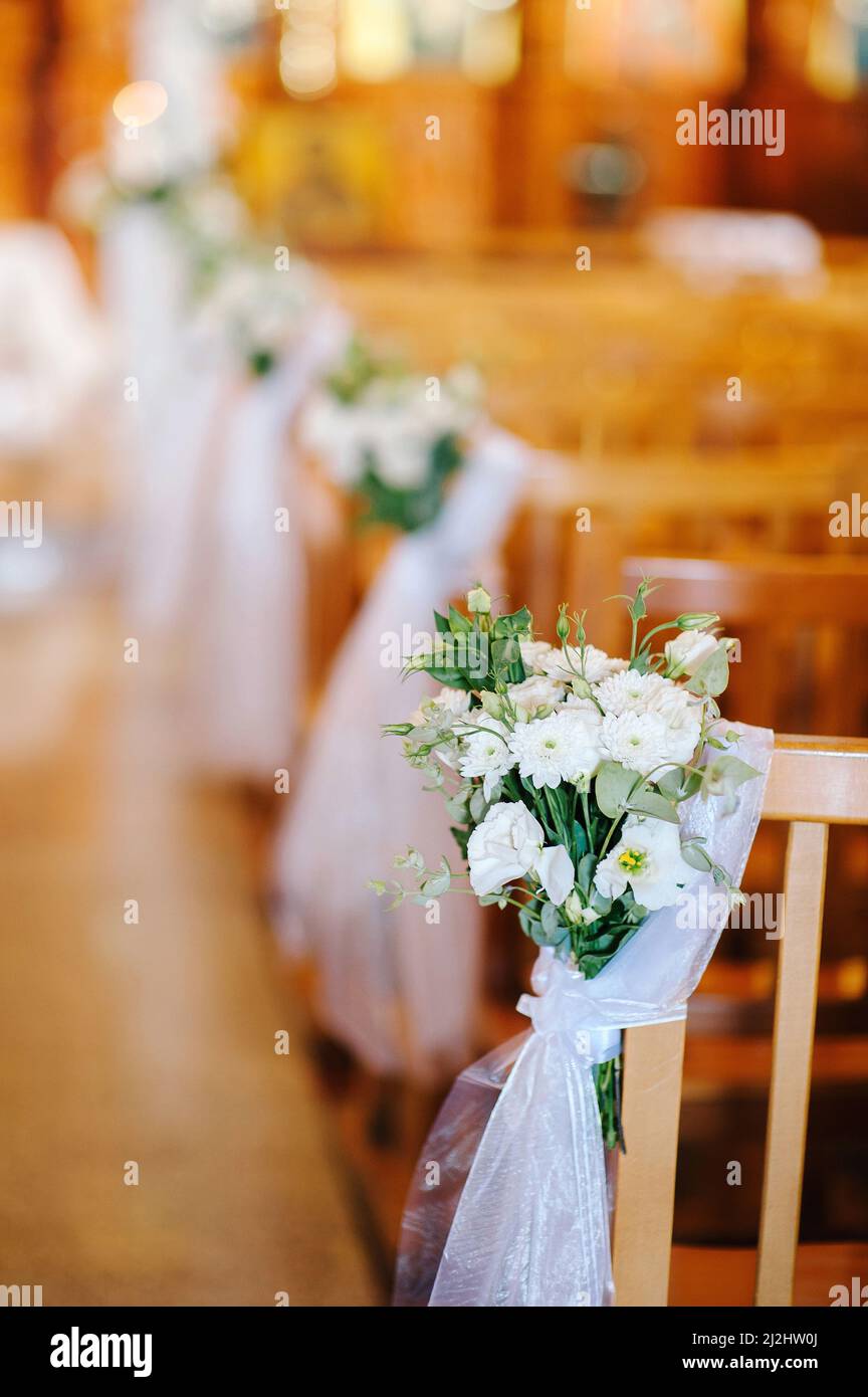 Wedding ceremony in church. Wooden chairs decorated with white tender ...