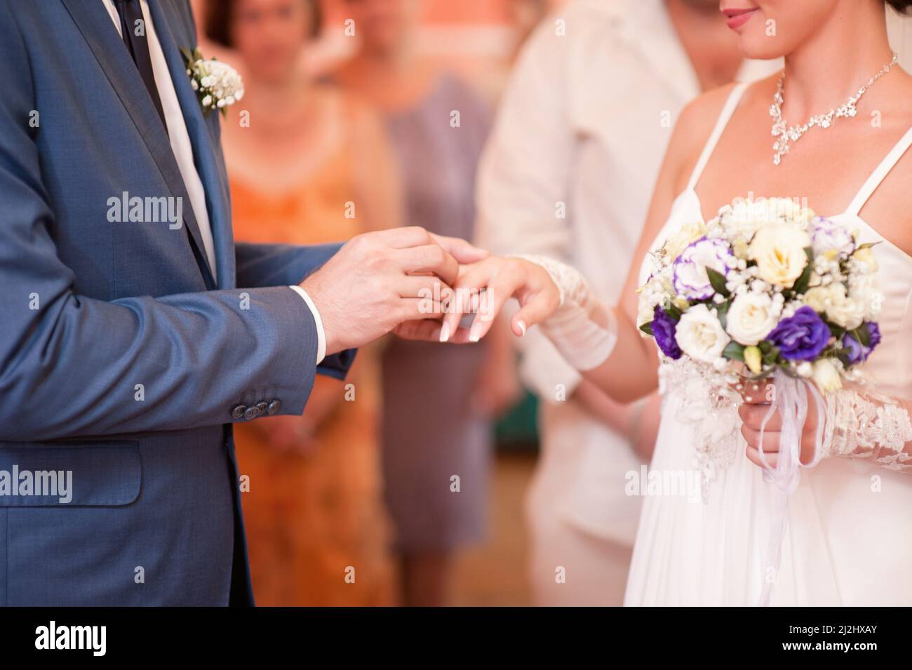 Wedding ceremony. Groom putting golden ring on bride's finger closeup