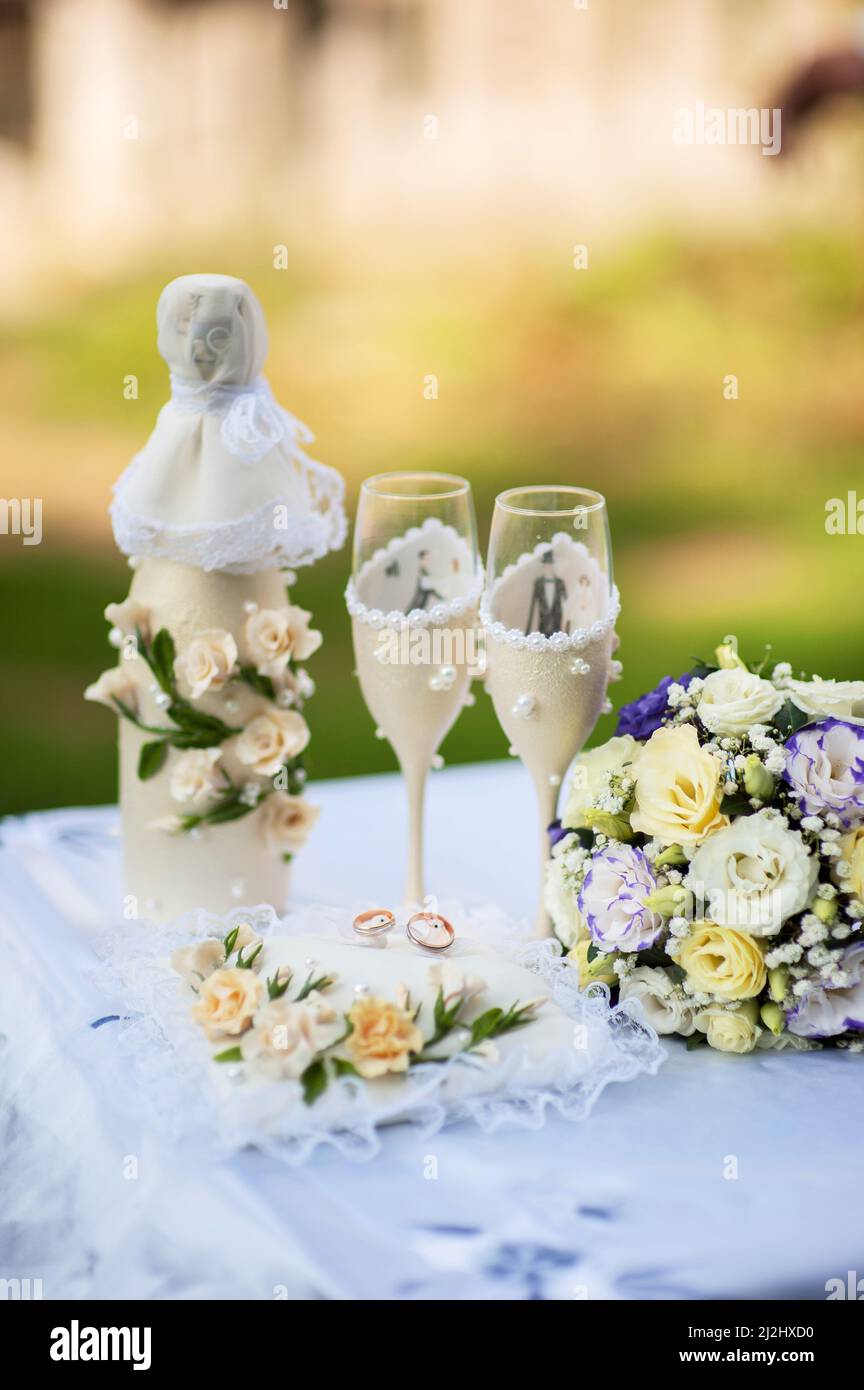 Bride's and groom's wedding wineglasses, bottle of champagne and bridal bouquet decorated with white flowers on ceremony table. Summer garden wedding Stock Photo