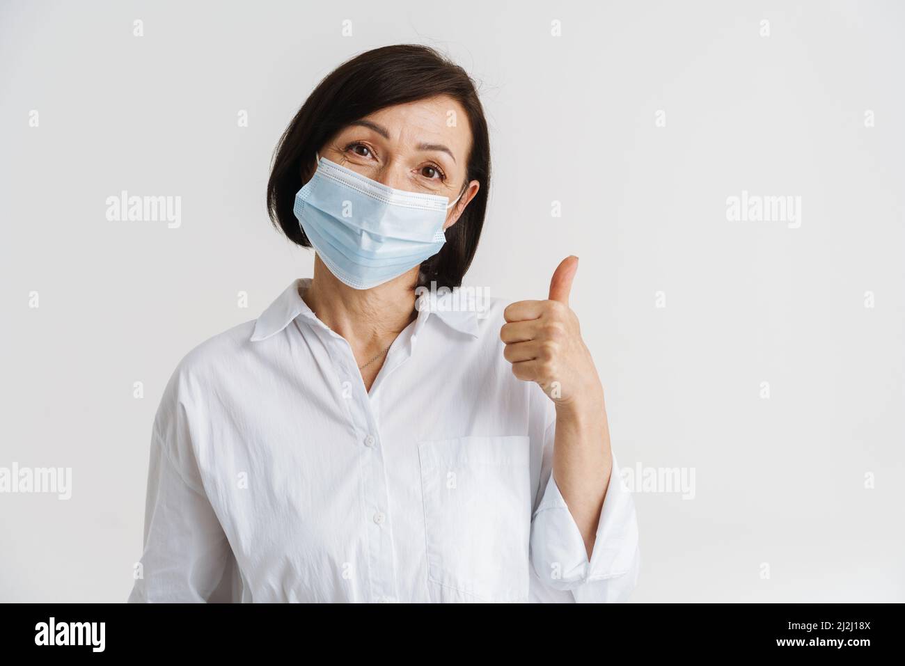 European mature woman in face mask showing thumb up isolated over white ...