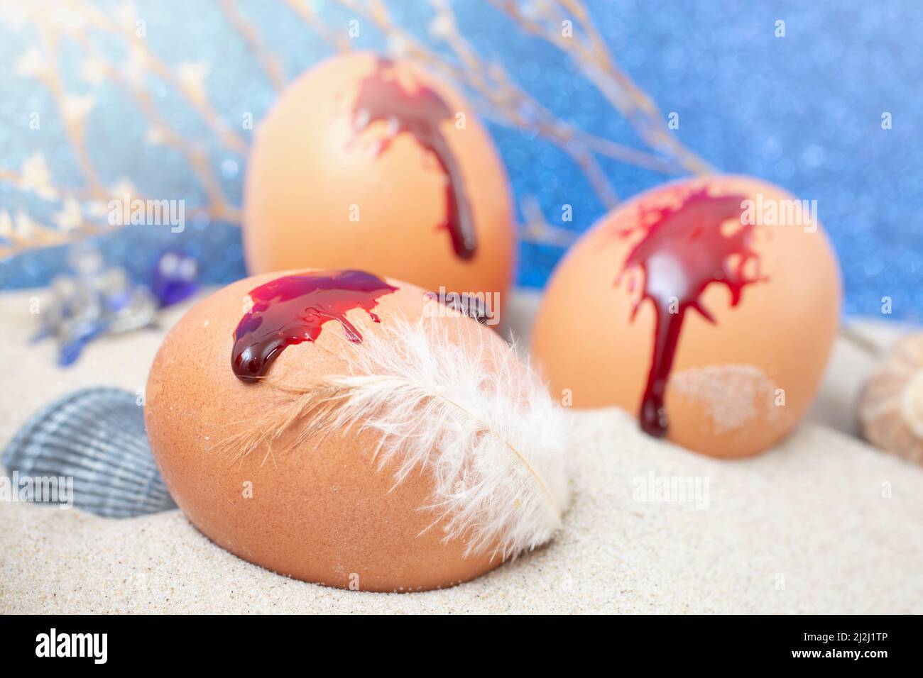 3 chicken eggs with blood and a feather, representing the blood of Jesus Christ, red eggs Easter tradition Stock Photo