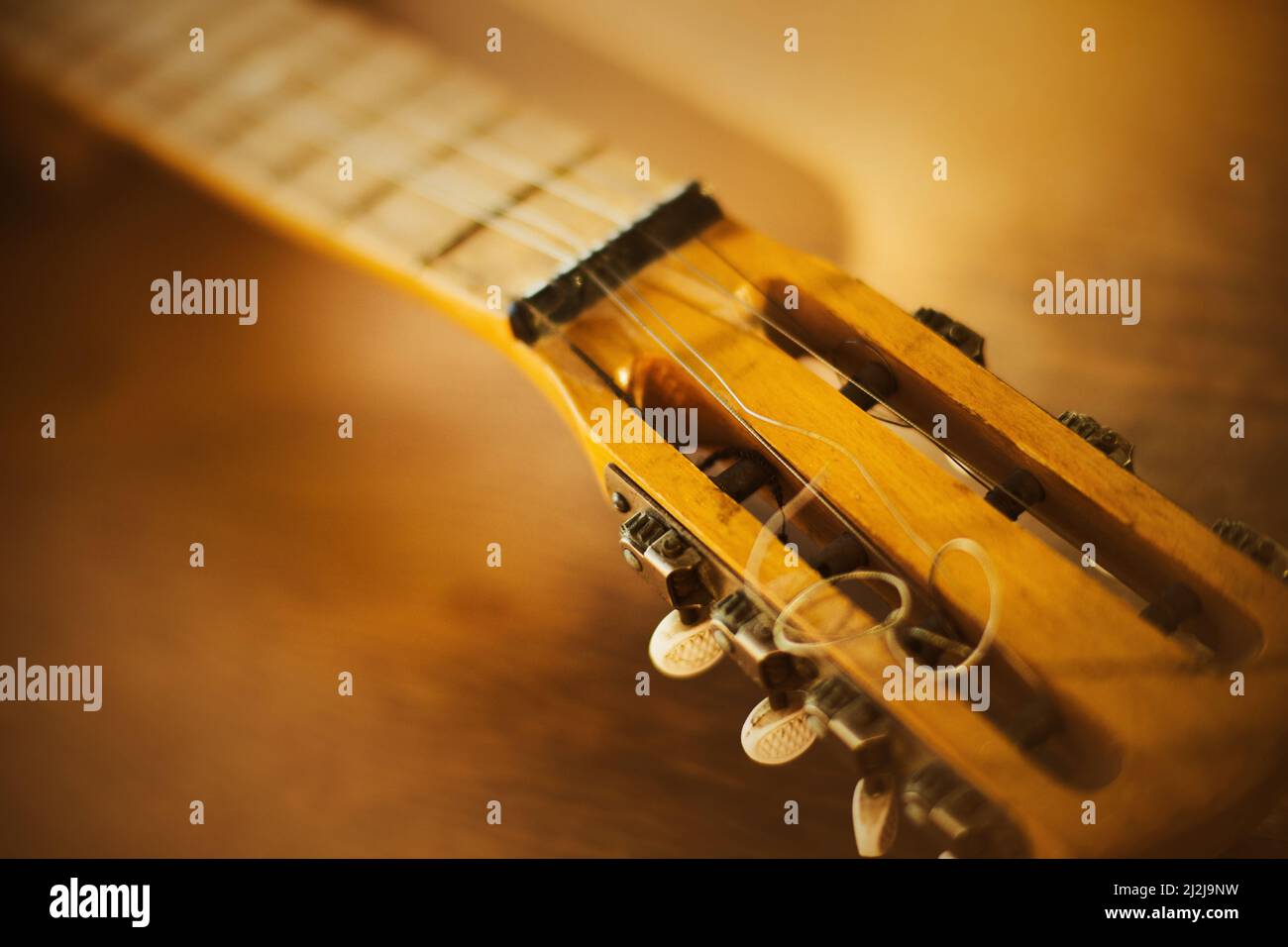 The neck of a beautiful vintage guitar with metal strings, which lies on a wooden table on a sunny day. Art and music. Solfeggio. Stock Photo