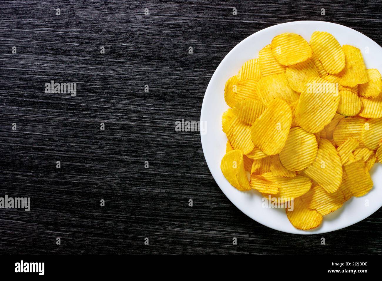 Potato chips chips in a white plate on a wooden table. Rustic food background. Top view. Copy space Stock Photo